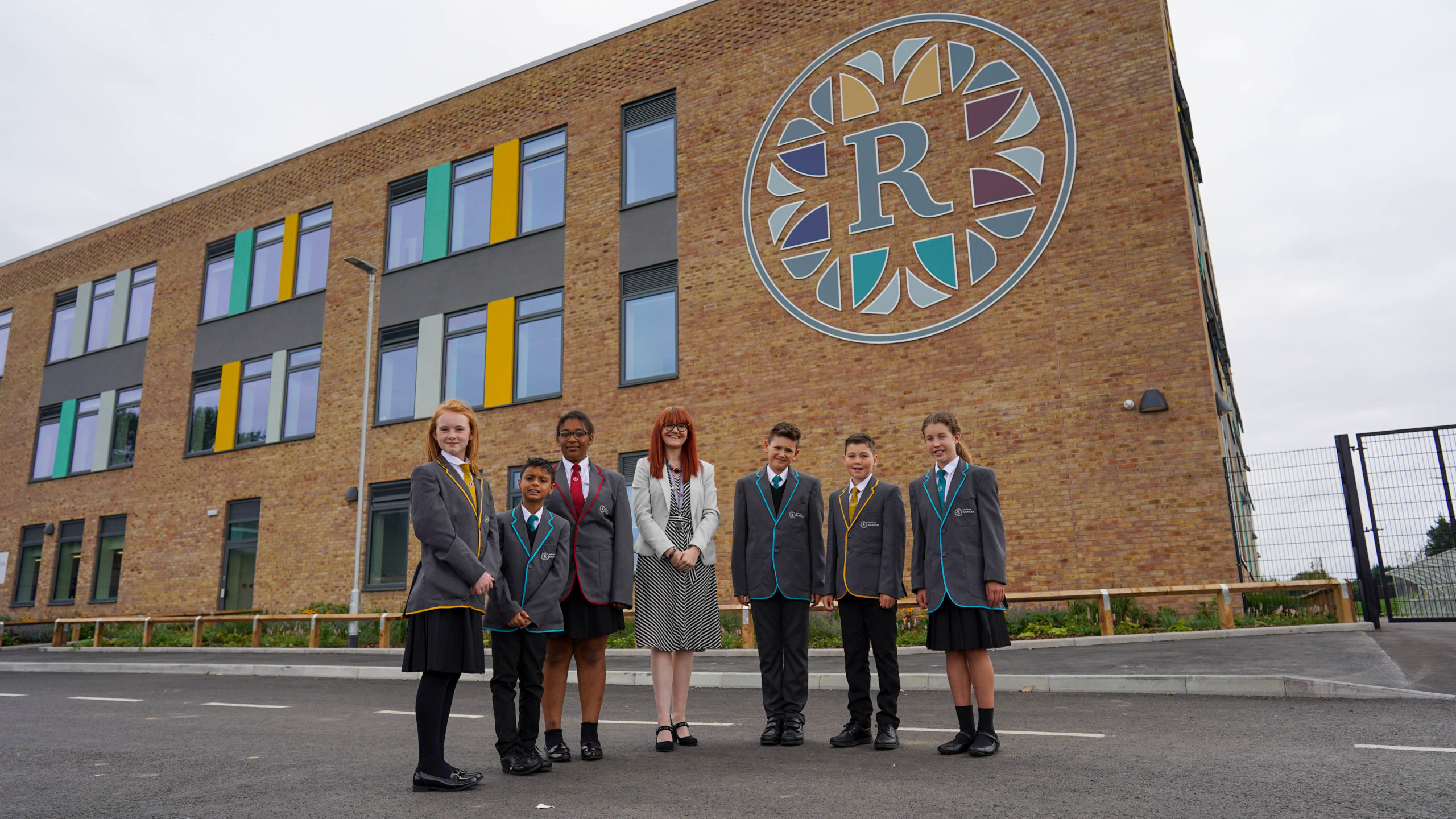 Six Leigh Academy Rainham students are seen posing for a photo outside the academy building, alongside the Principal, Alex Millward.