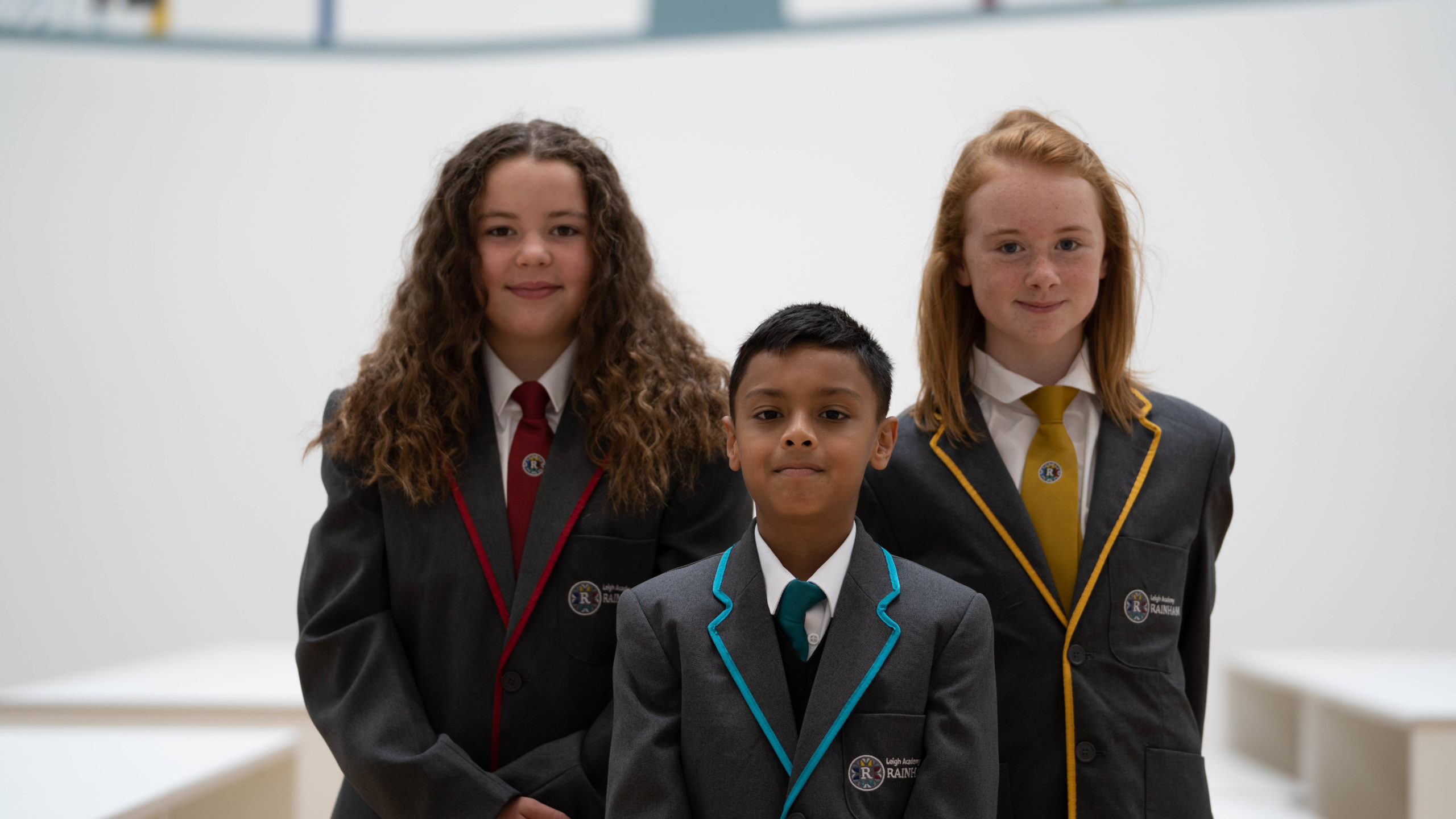 Two girls and a boy are seen posing together for a photo, wearing their school uniform, each with a different colour stripe to represent the academy's three colleges.