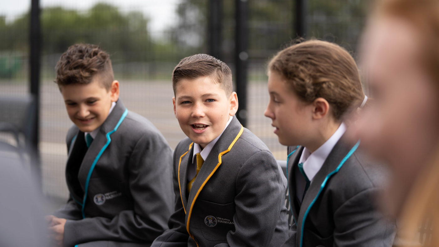 Three Leigh Academy Rainham students are pictured on the academy grounds, smiling for the camera, wearing their school uniform.