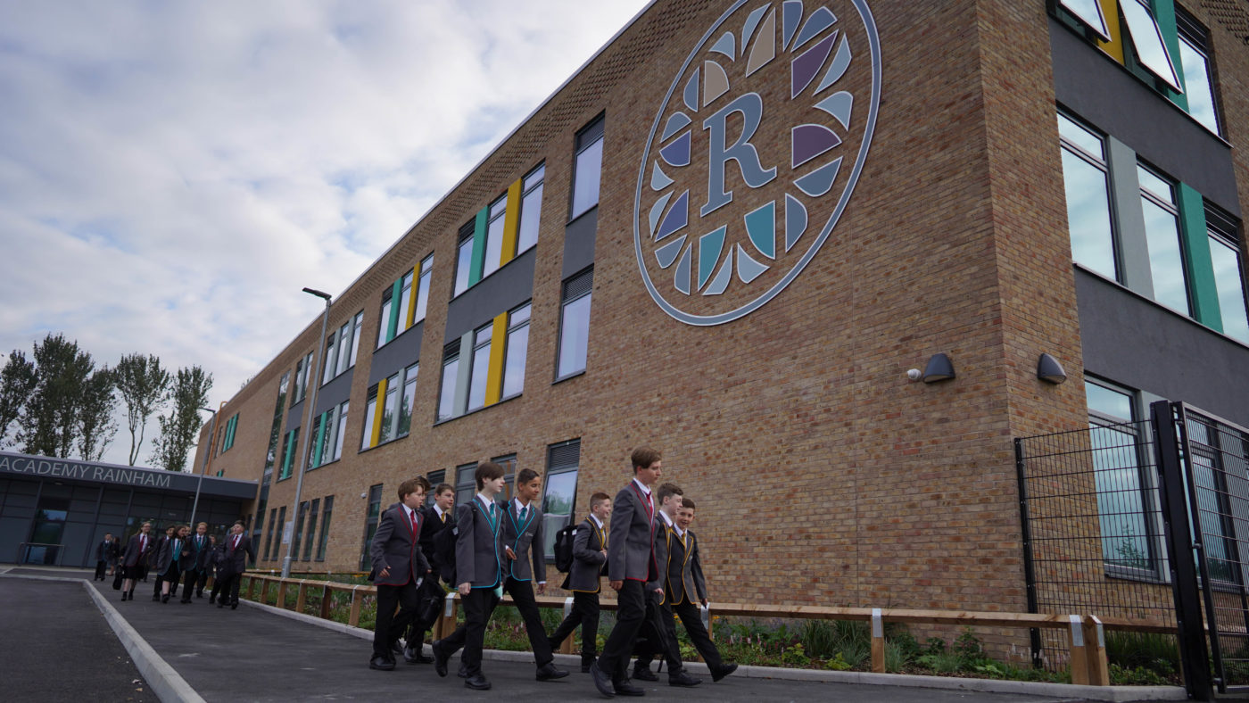 A group of students are seen walking past the academy building at the end of the school day.
