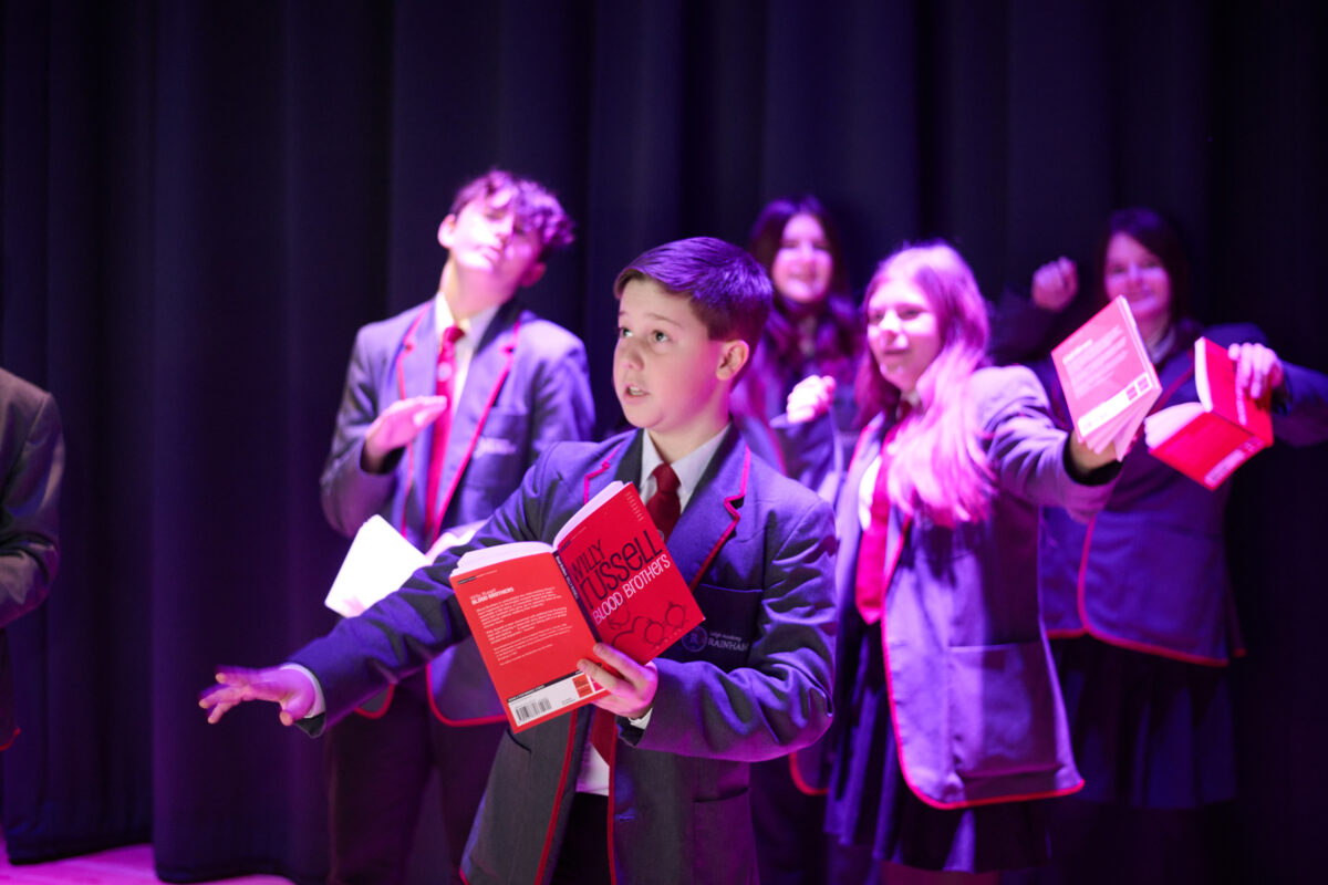 5 students on stage acting, holding a book of Blood Brothers