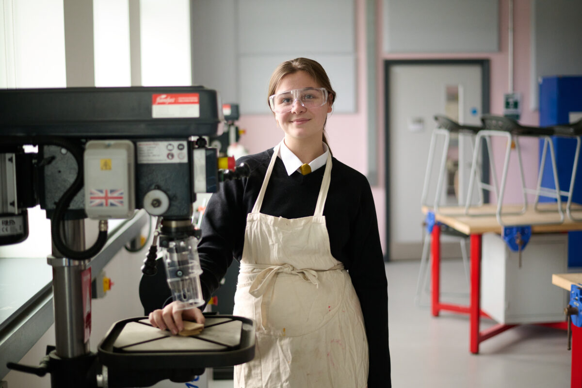 A student in an apron and goggles smiling for the camera
